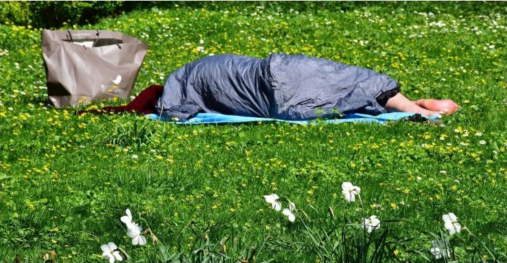 czlowiek leżący w parku pod śpiworem