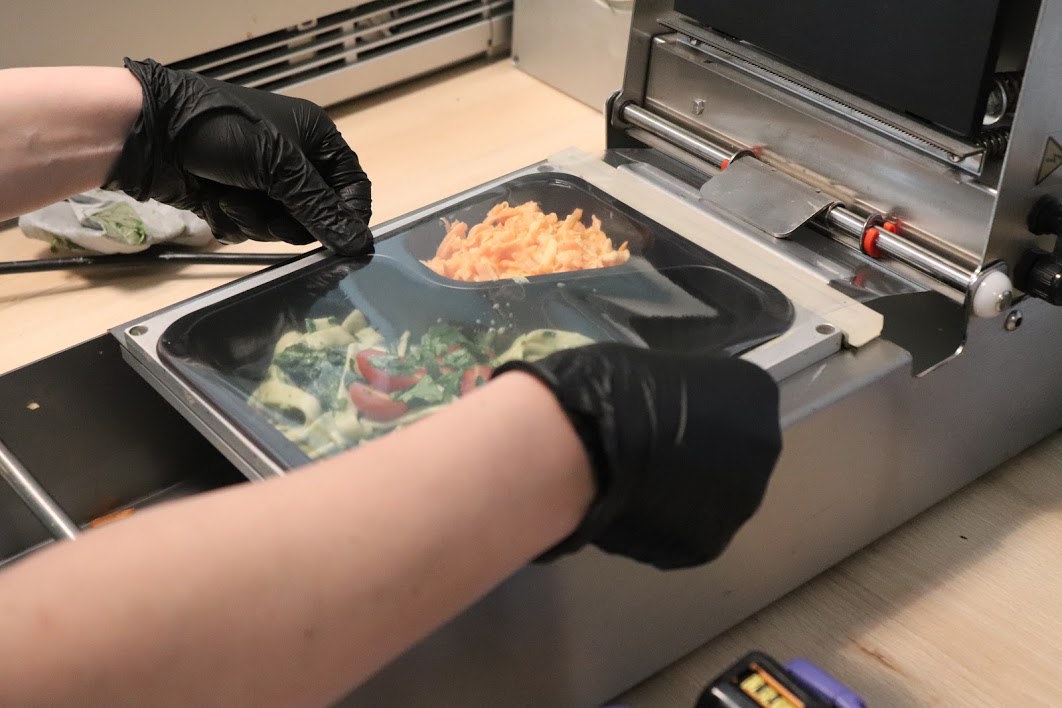 zdjęcie przedstawia ciepły posiłek na naczyniu podawany przez pracownika w ochronnych rękawiczkach
